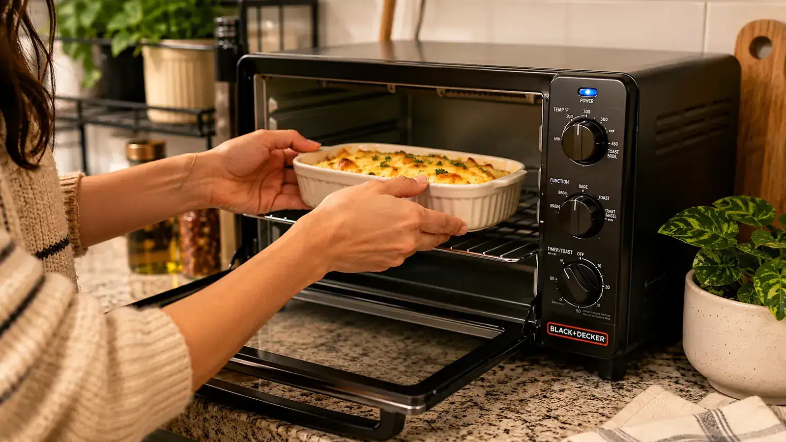 A hand sliding a small baking dish into the BLACK+DECKER toaster oven