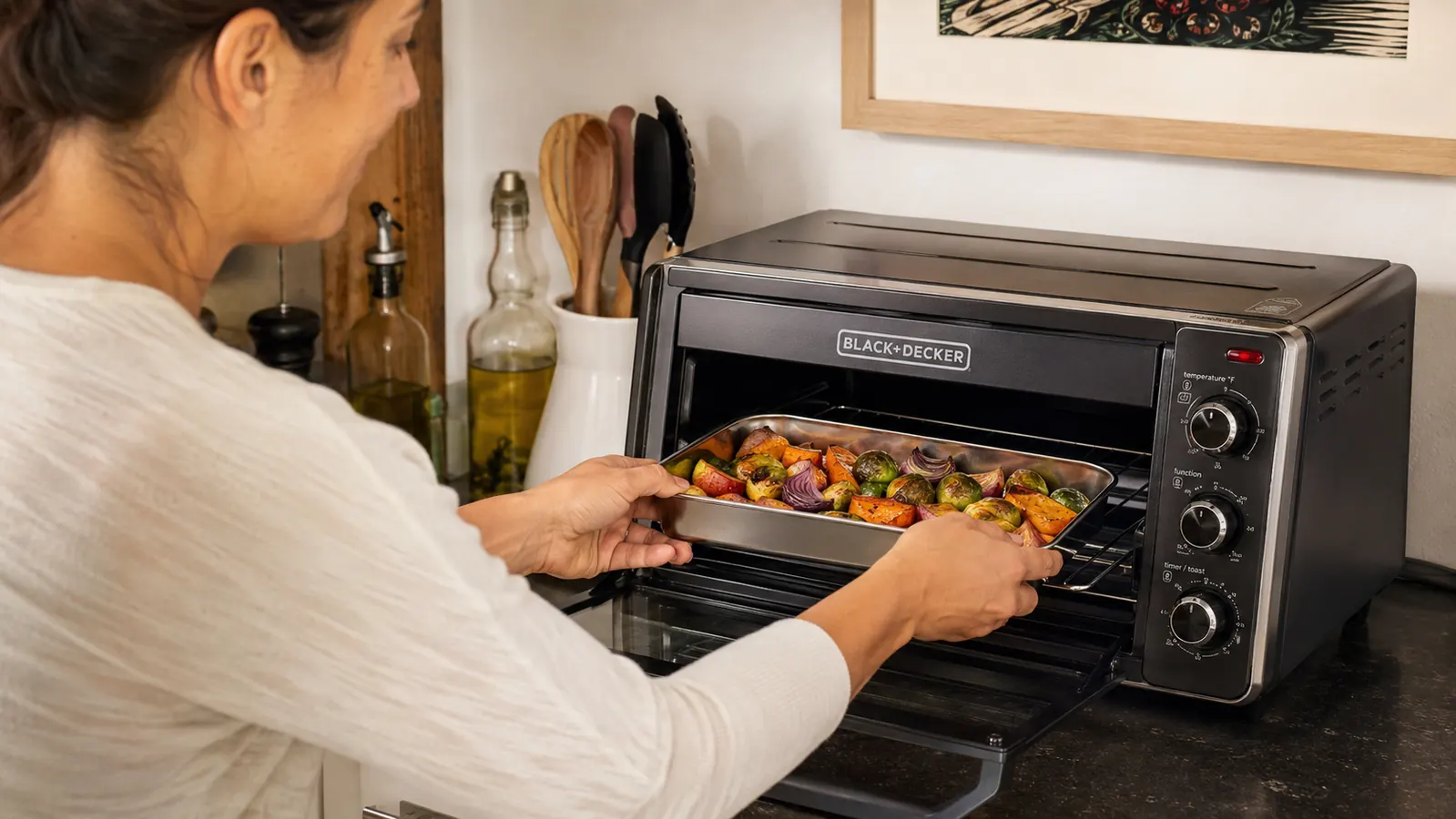 Person placing a small baking pan into a toaster oven in a tight apartment kitchen