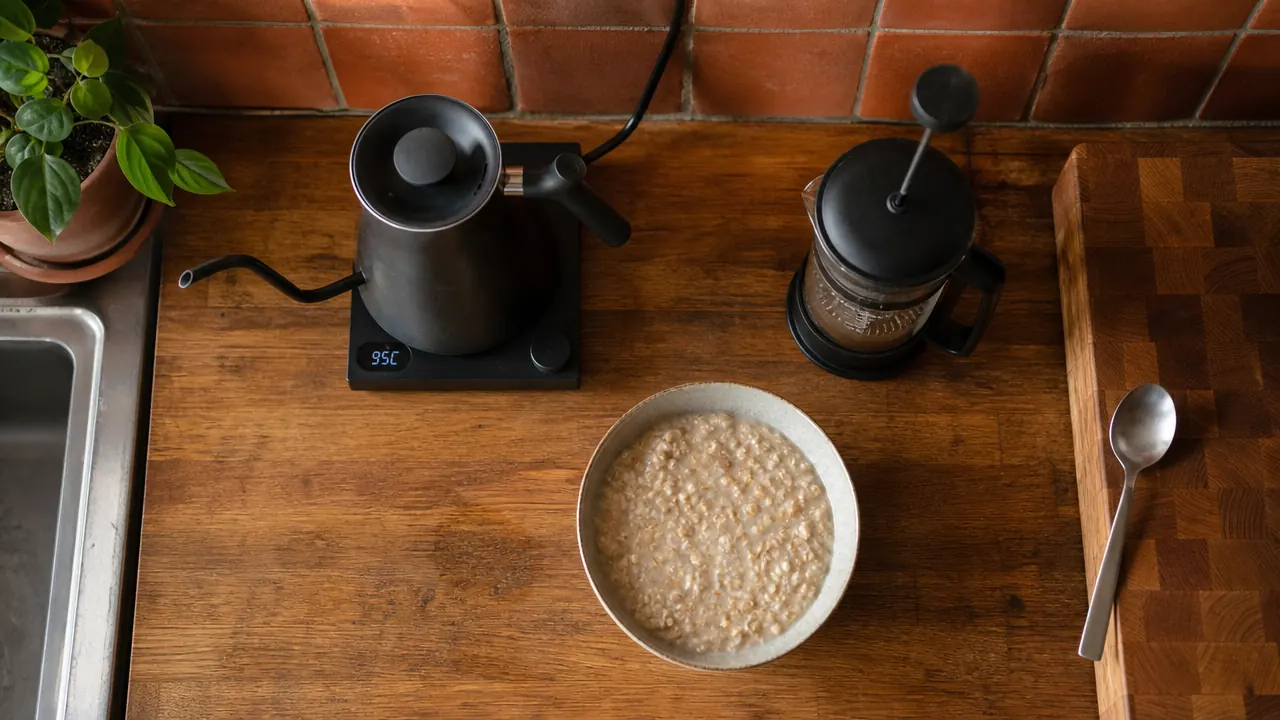 Top-down view of the Mueller electric kettle sitting on its base beside a bowl of instant oatmeal and a French press on a small counter